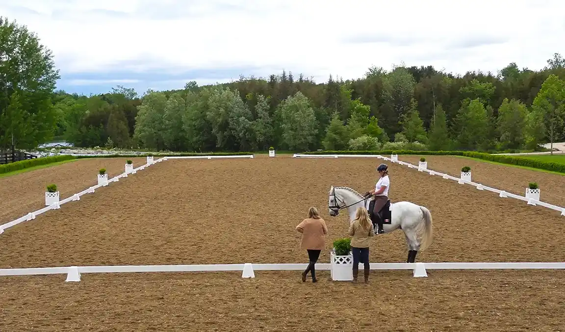 Dust-Free dressage outdoor arena. Trainer and rider on grey horse.